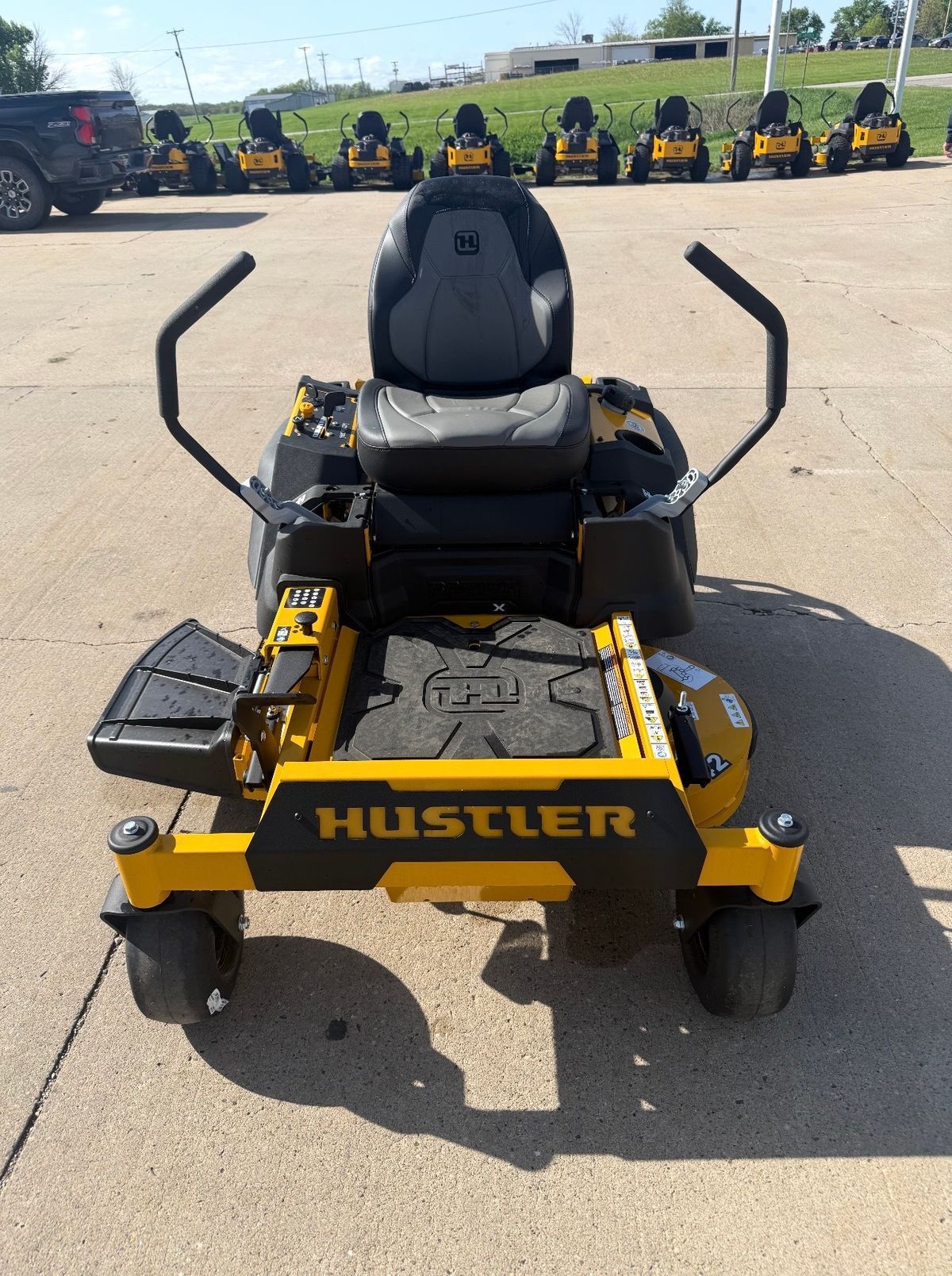 Front view of a yellow Hustler zero-turn mower parked on pavement outdoors
