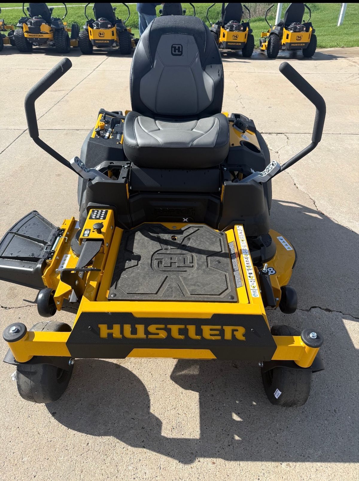 Black Hustler zero-turn lawn mower parked on pavement, front view with yellow deck and frame.