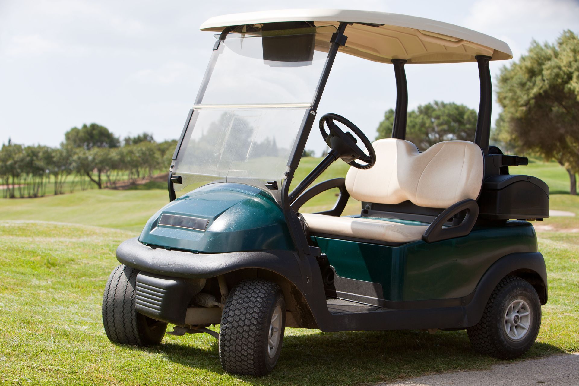 Green golf cart with beige roof and seats parked on grass in a sunny outdoor setting