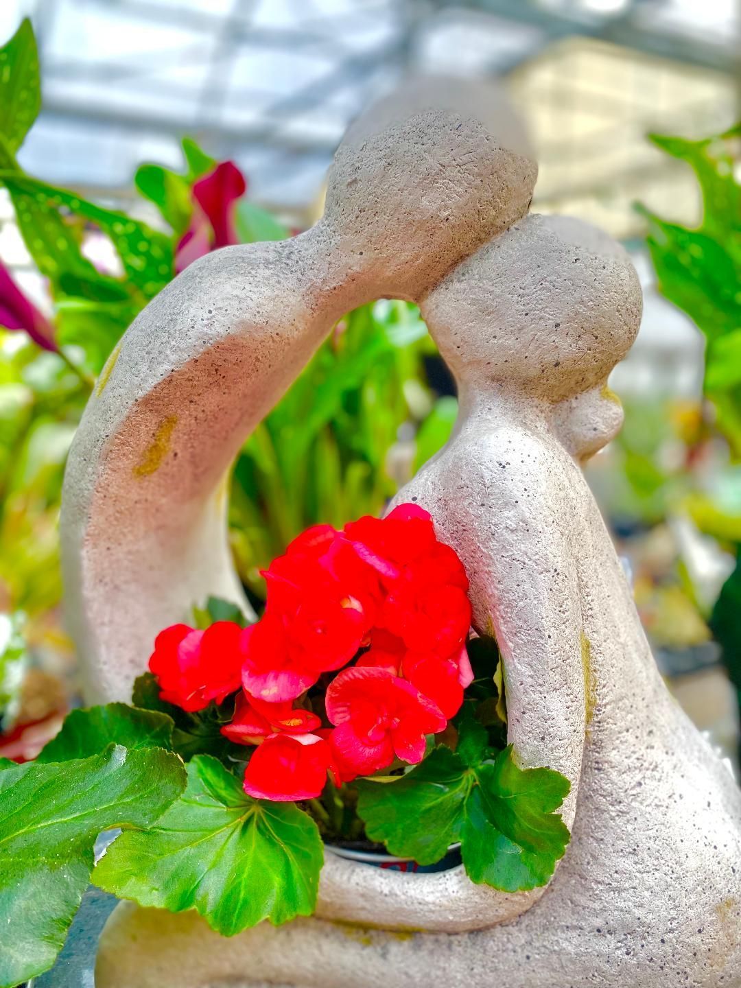 A statue of two people hugging each other with red flowers in the middle
