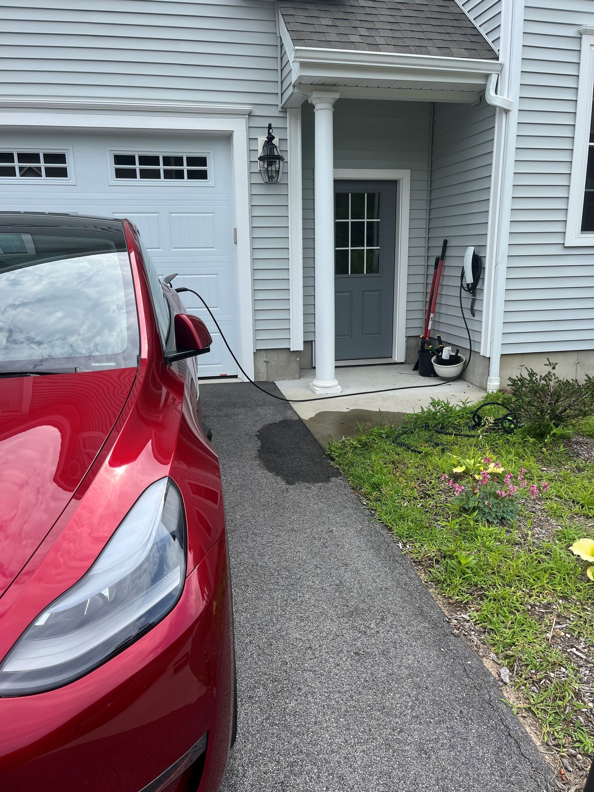 A red tesla model y is parked in front of a white house.