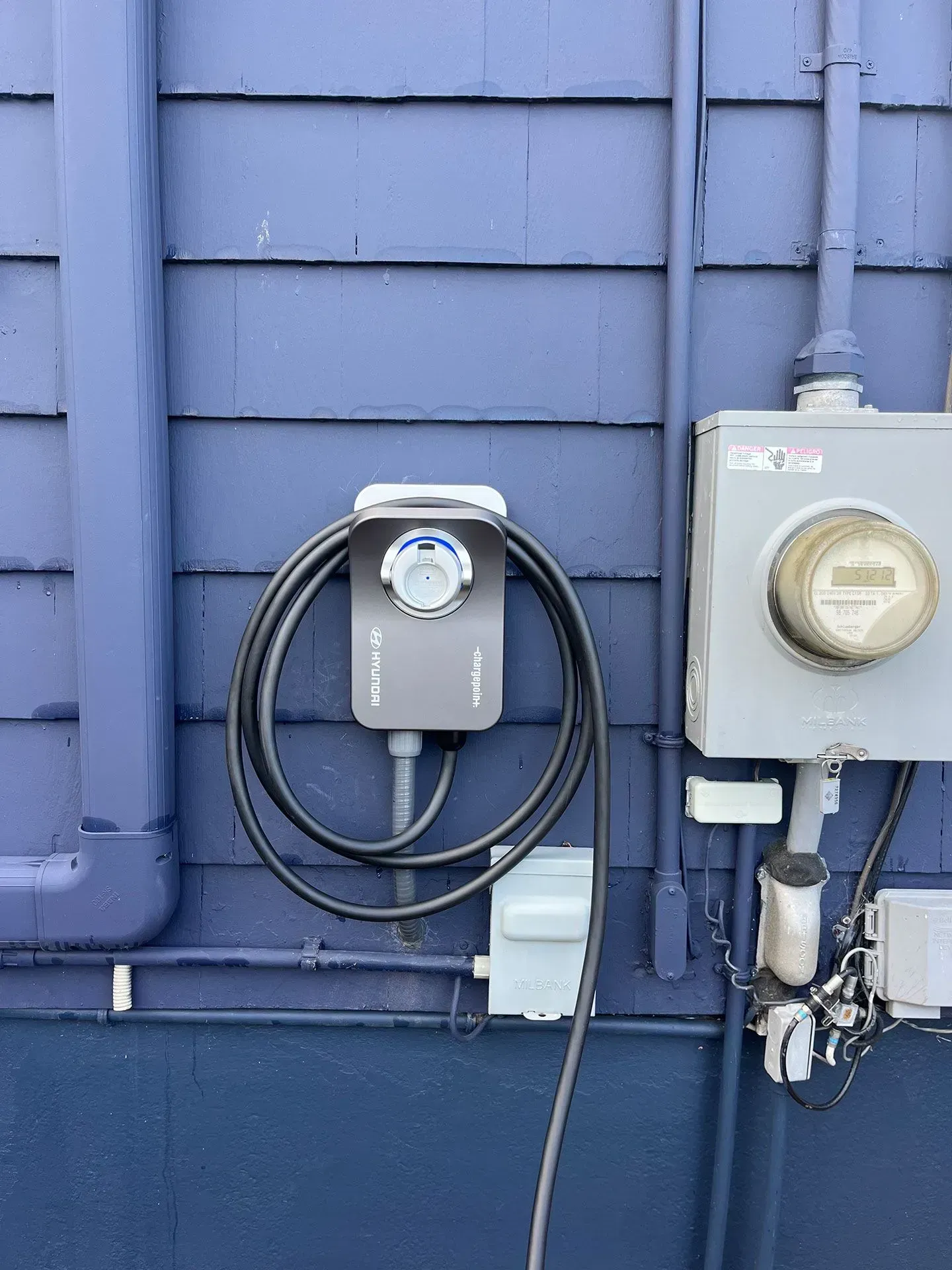 A black cord is connected to a electrical box on the side of a building.