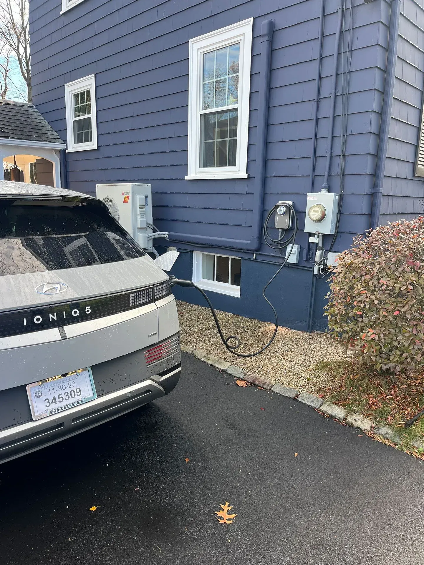 A car is being charged in front of a blue house.