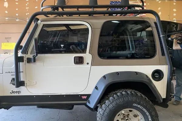White Jeep Wrangler with black fender flares and roof rack, parked indoors.