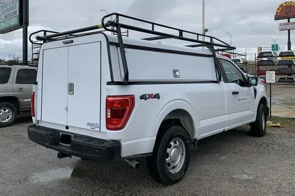 White pickup truck with canopy and roof rack parked on a gravel lot