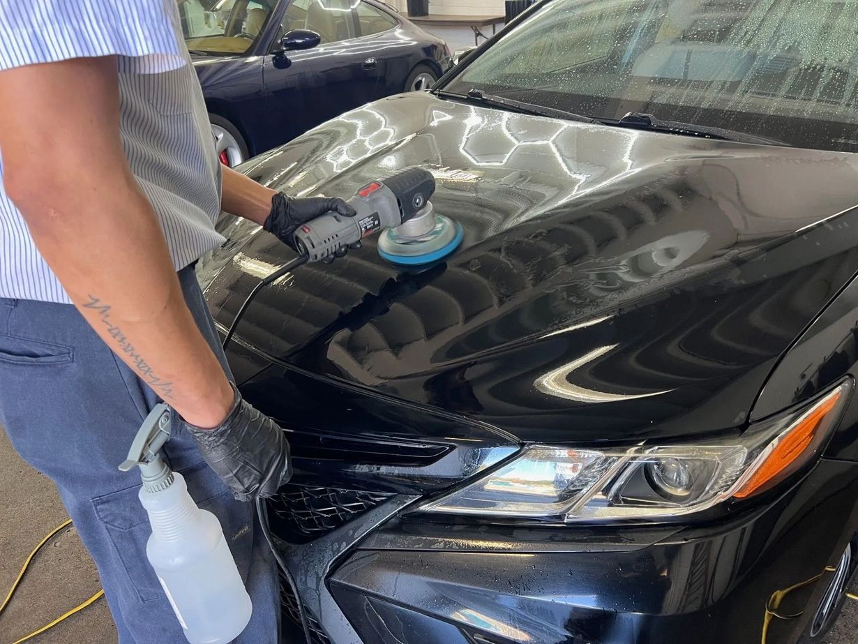 Person polishing a black car hood with a buffer in a garage