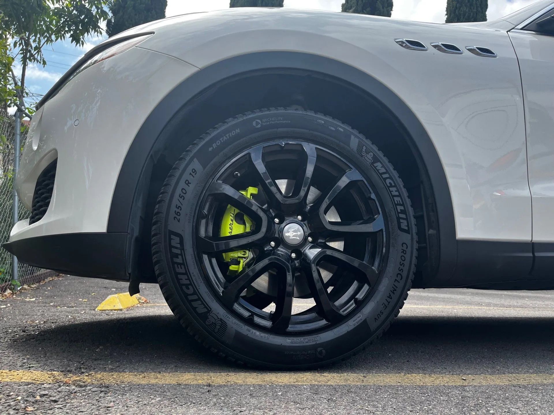 A close-up of a white Maserati’s front wheel featuring black rims and a bright yellow brake caliper.