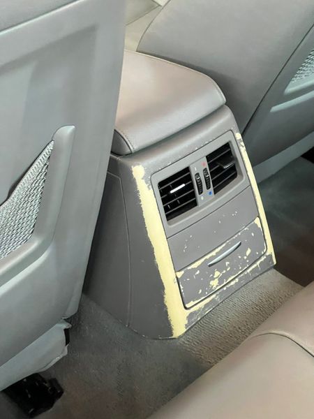 The gray center console in a car’s backseat is worn and peeling, showing a lighter yellow underlayer.