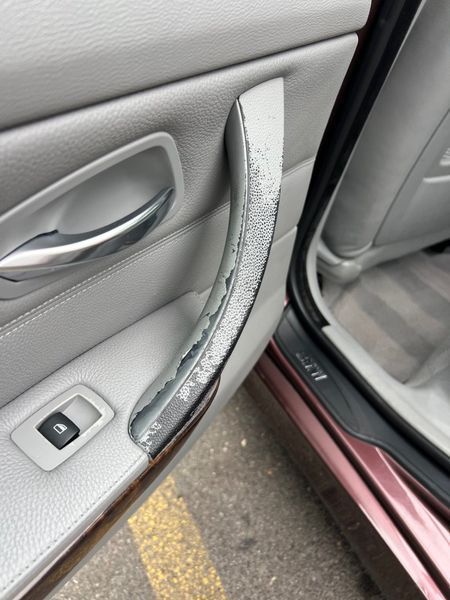 Close-up of a worn grey car interior door handle with peeling paint, showing damage to the plastic grip.