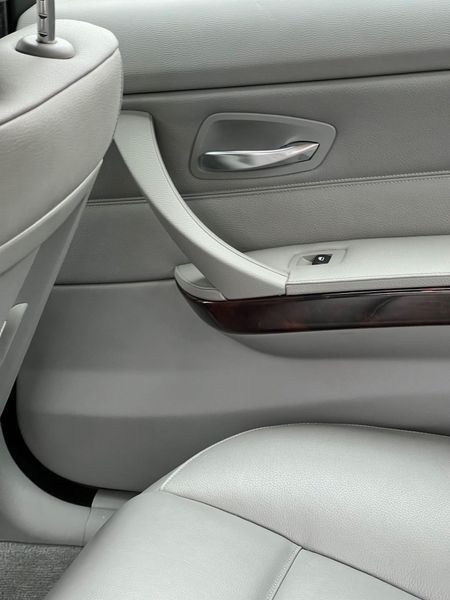 A close-up interior view of a gray leather car door panel with a silver handle, wood trim, and part of a passenger seat.