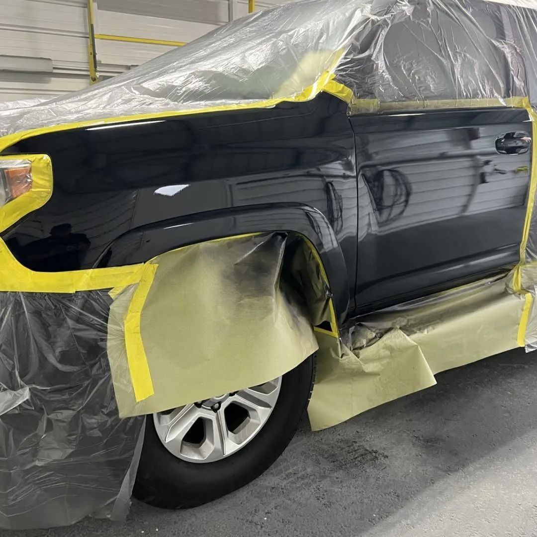 A black truck fender and door masked with tape and plastic sheeting in an auto body shop, prepared for painting.
