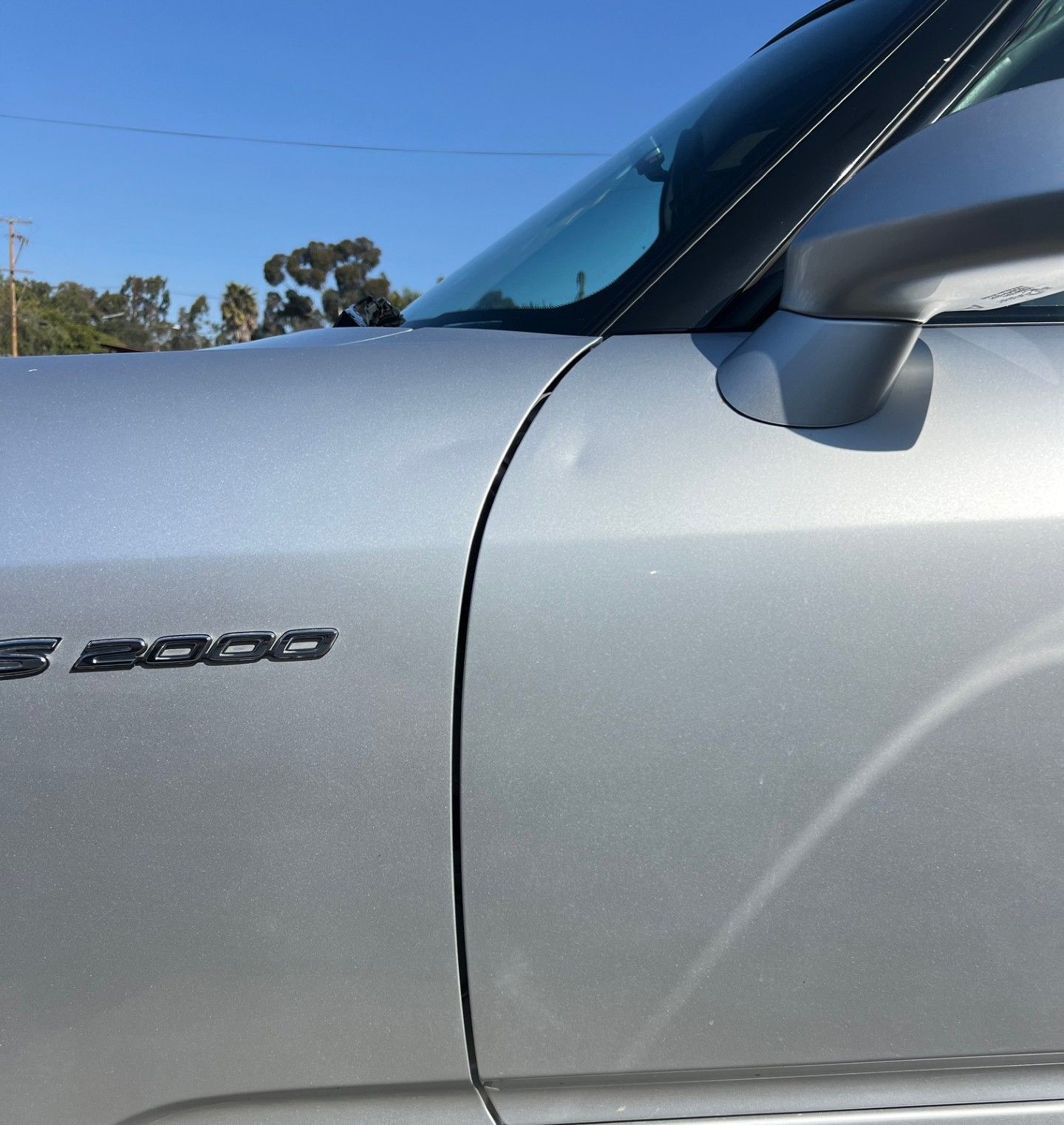 A close-up view of a silver S2000 car's side, showing a small dent on the door panel near the fender seam.