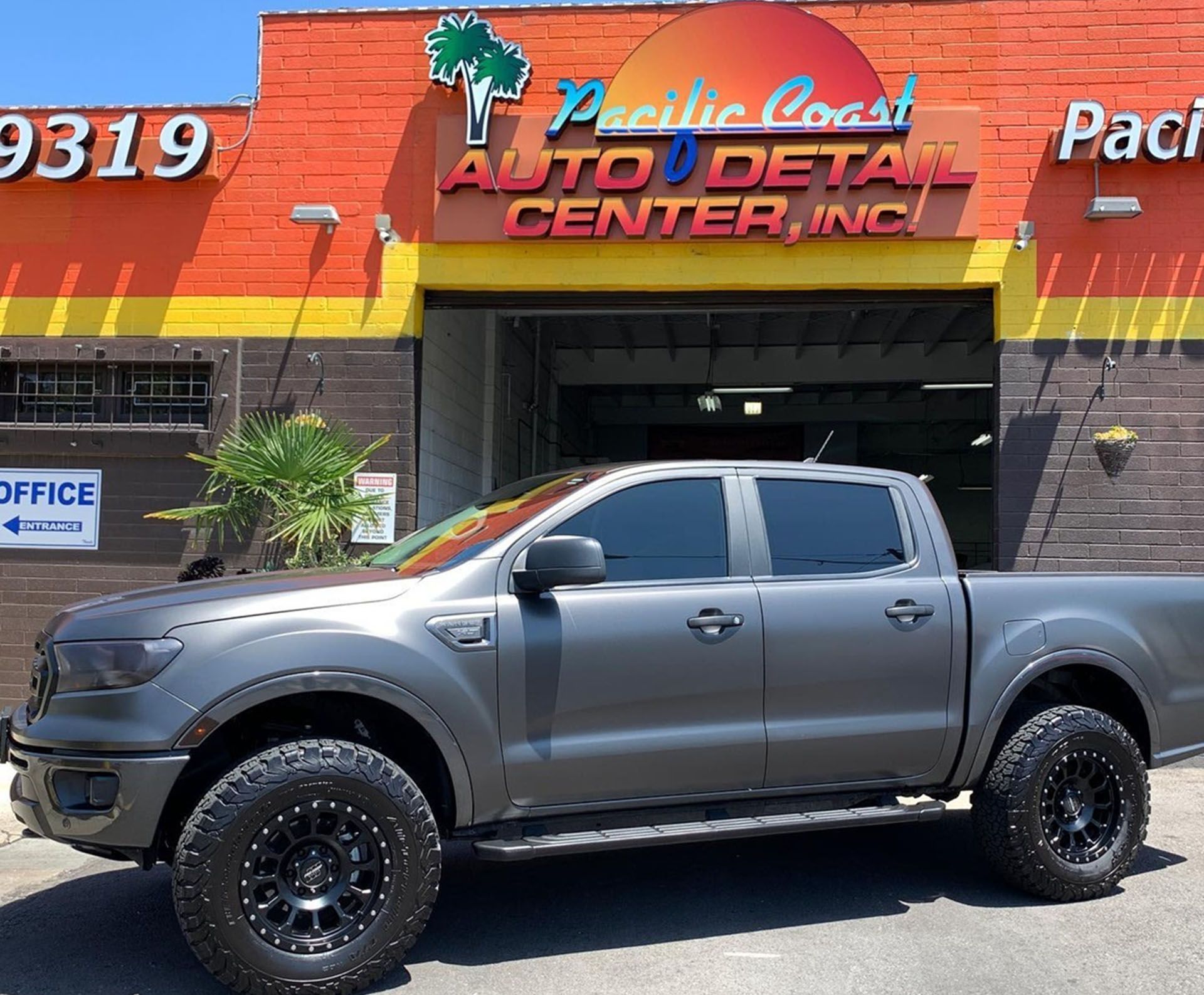A gray Ford Ranger truck with off-road tires parked in front of the Pacific Coast Auto Detail Center.