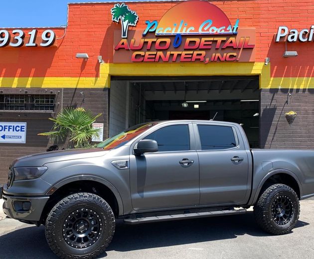 A dark gray Ford Ranger pickup truck with off-road tires parked in front of the Pacific Coast Auto Detail Center.