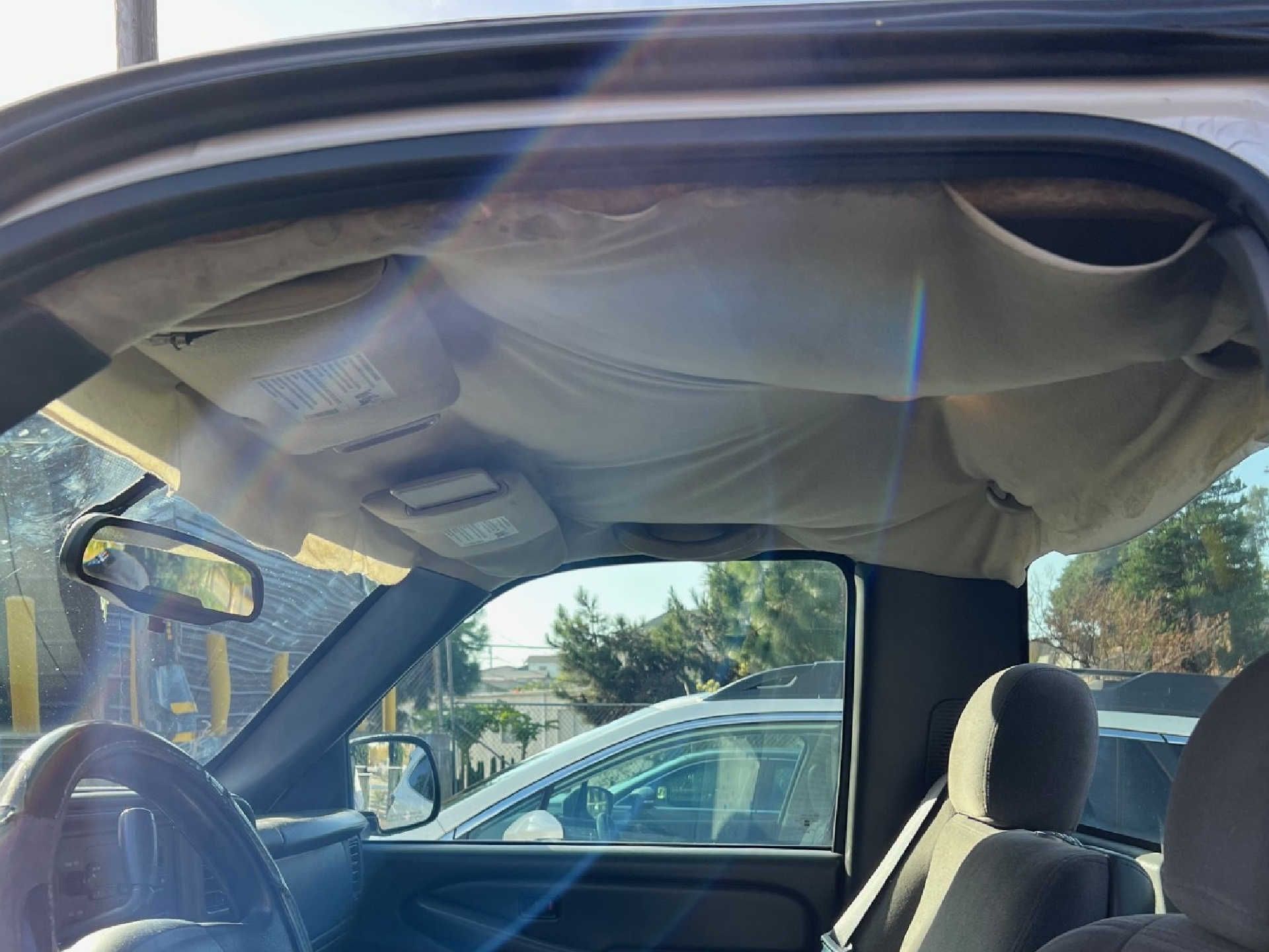 The fabric headliner in a vehicle interior is detached and sagging from the roof.