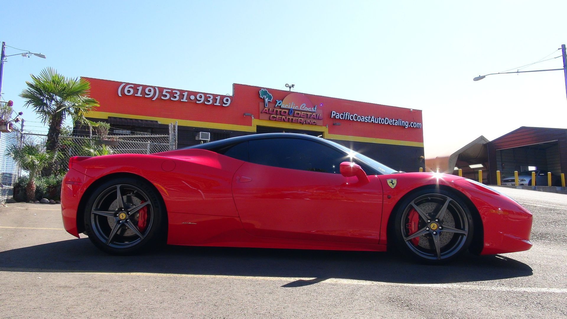 A red Ferrari parked in front of an orange commercial building on a sunny day.