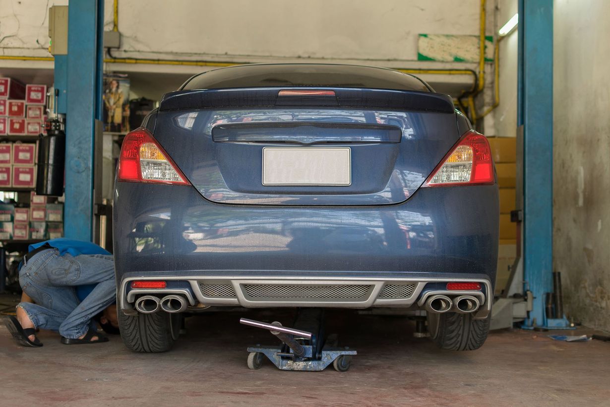 Blue car lifted in a garage for repair, with a mechanic working near the rear wheel
