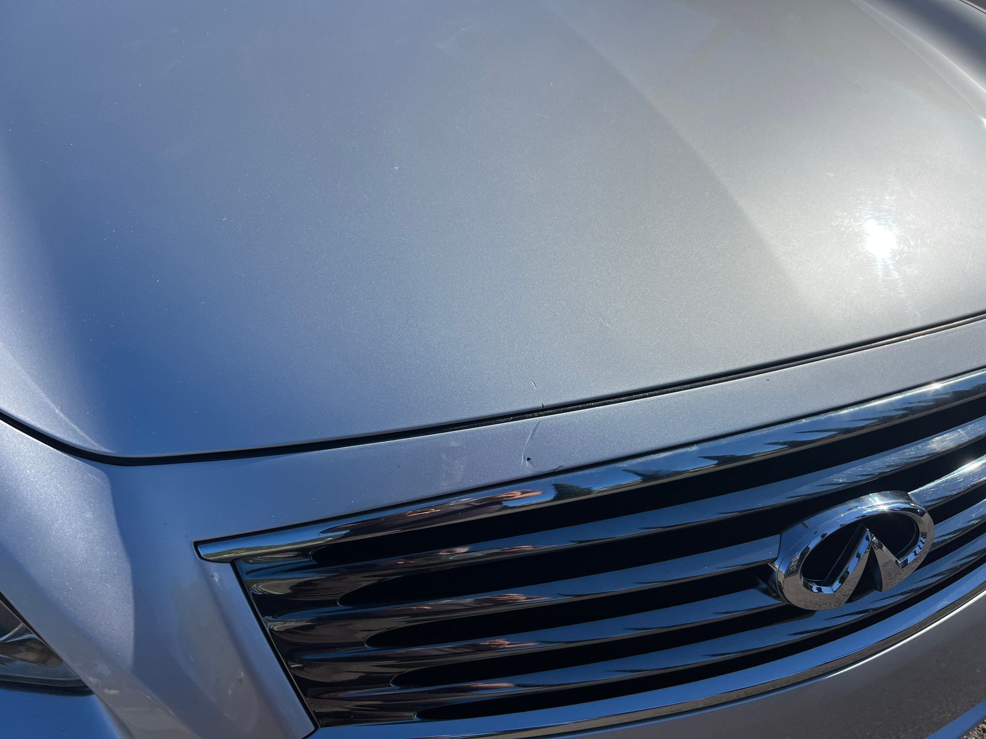 Close-up view of the front hood and black grille of a silver Infiniti car, showing the brand's logo.
