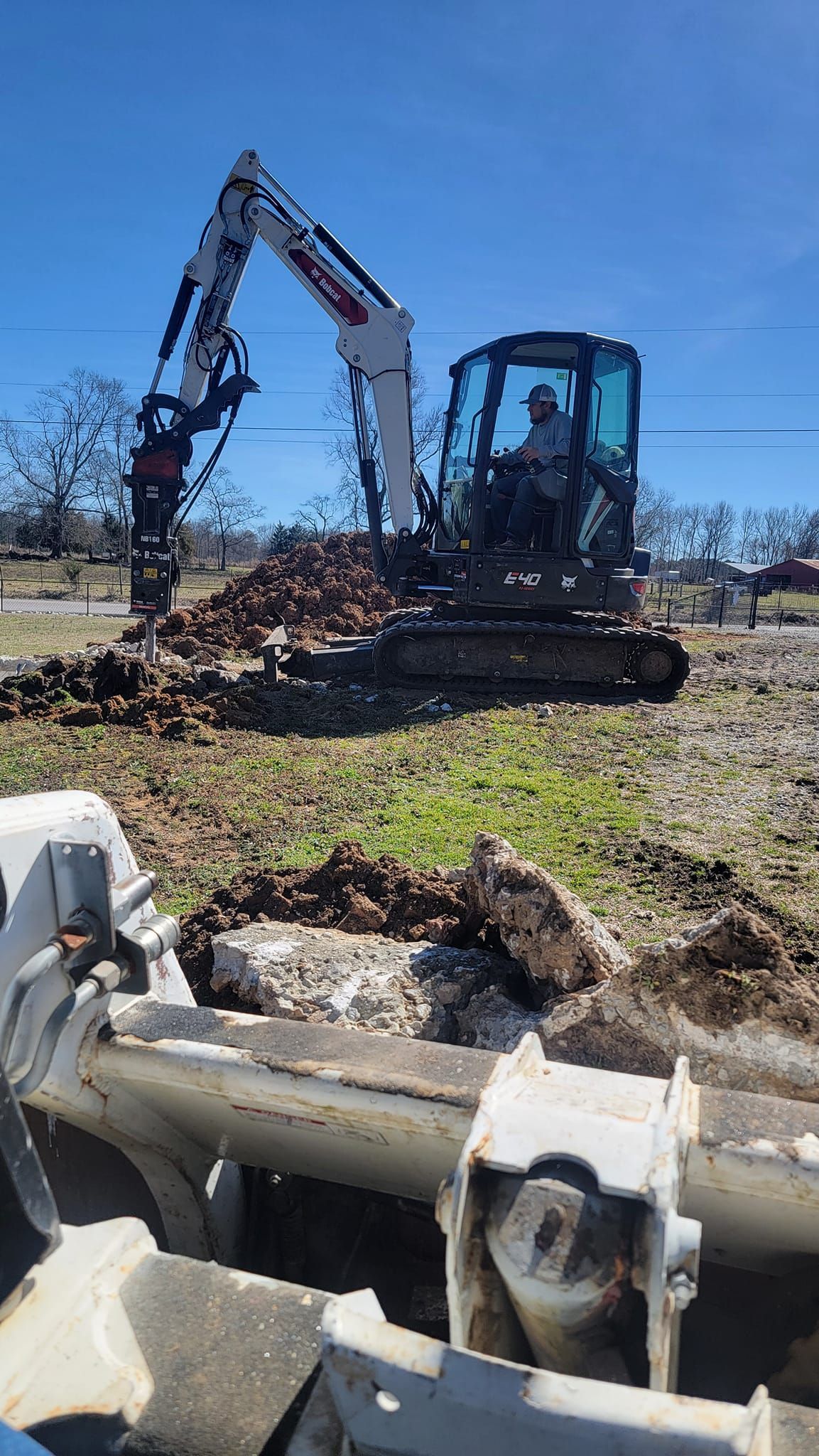 A man is driving an excavator in a field.