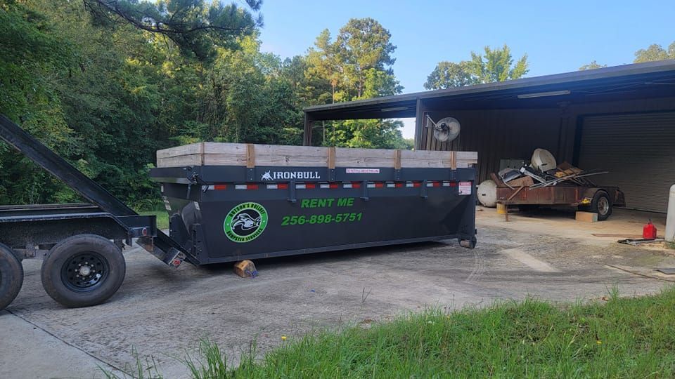 A dumpster is sitting on top of a trailer in front of a building.