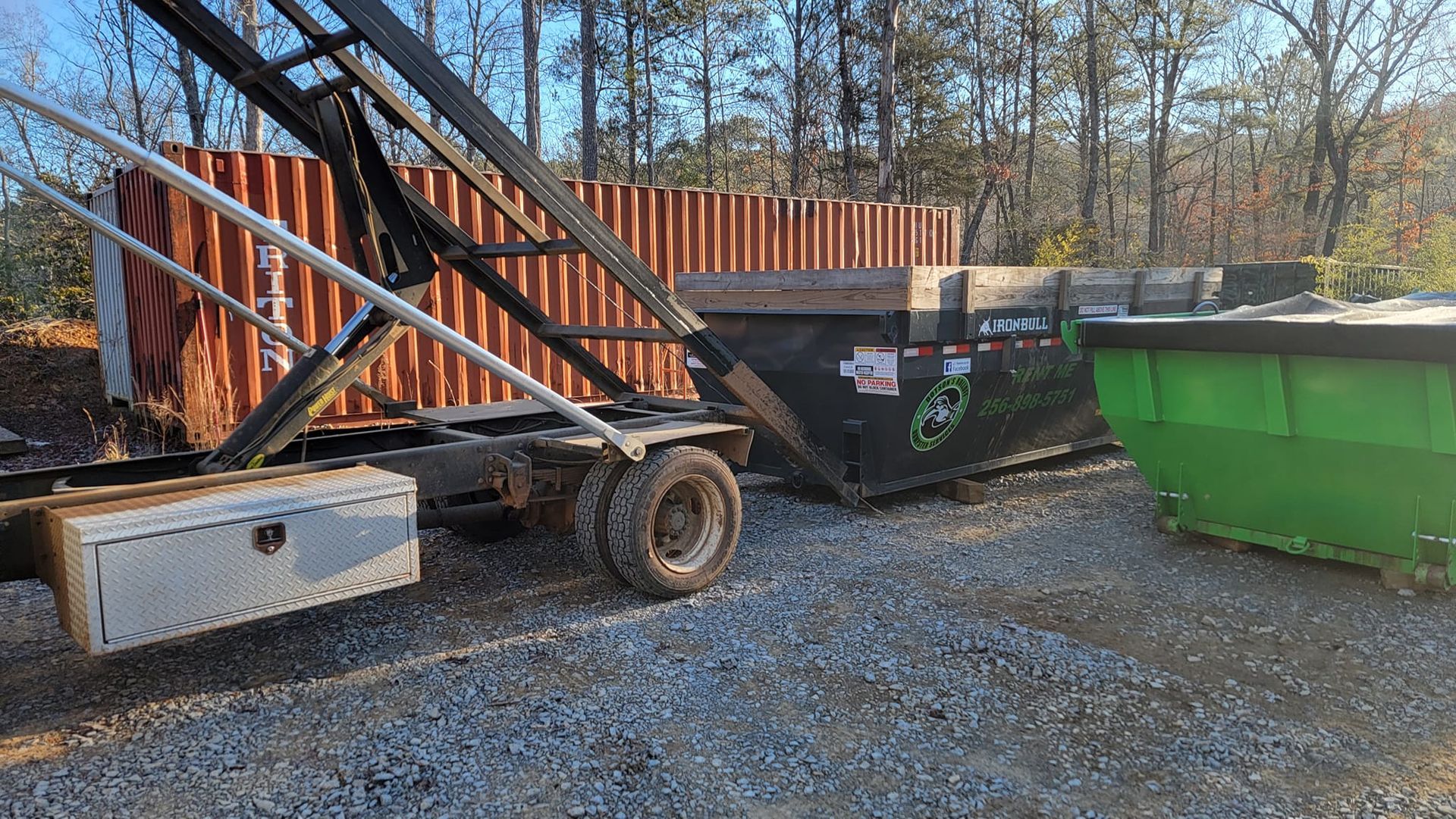 A dumpster is sitting next to a truck in a gravel lot.