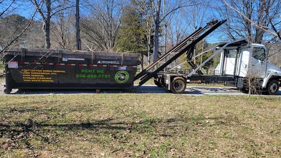White truck with a raised dump bed beside a black trailer in a grassy yard on a sunny day