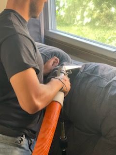 A man is cleaning a couch with a vacuum cleaner.