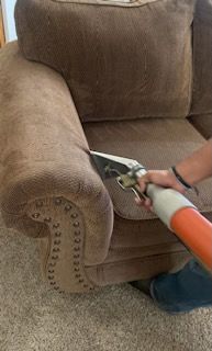 A person is cleaning a couch with a vacuum cleaner