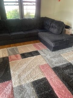 A living room with a black sectional couch and a rug