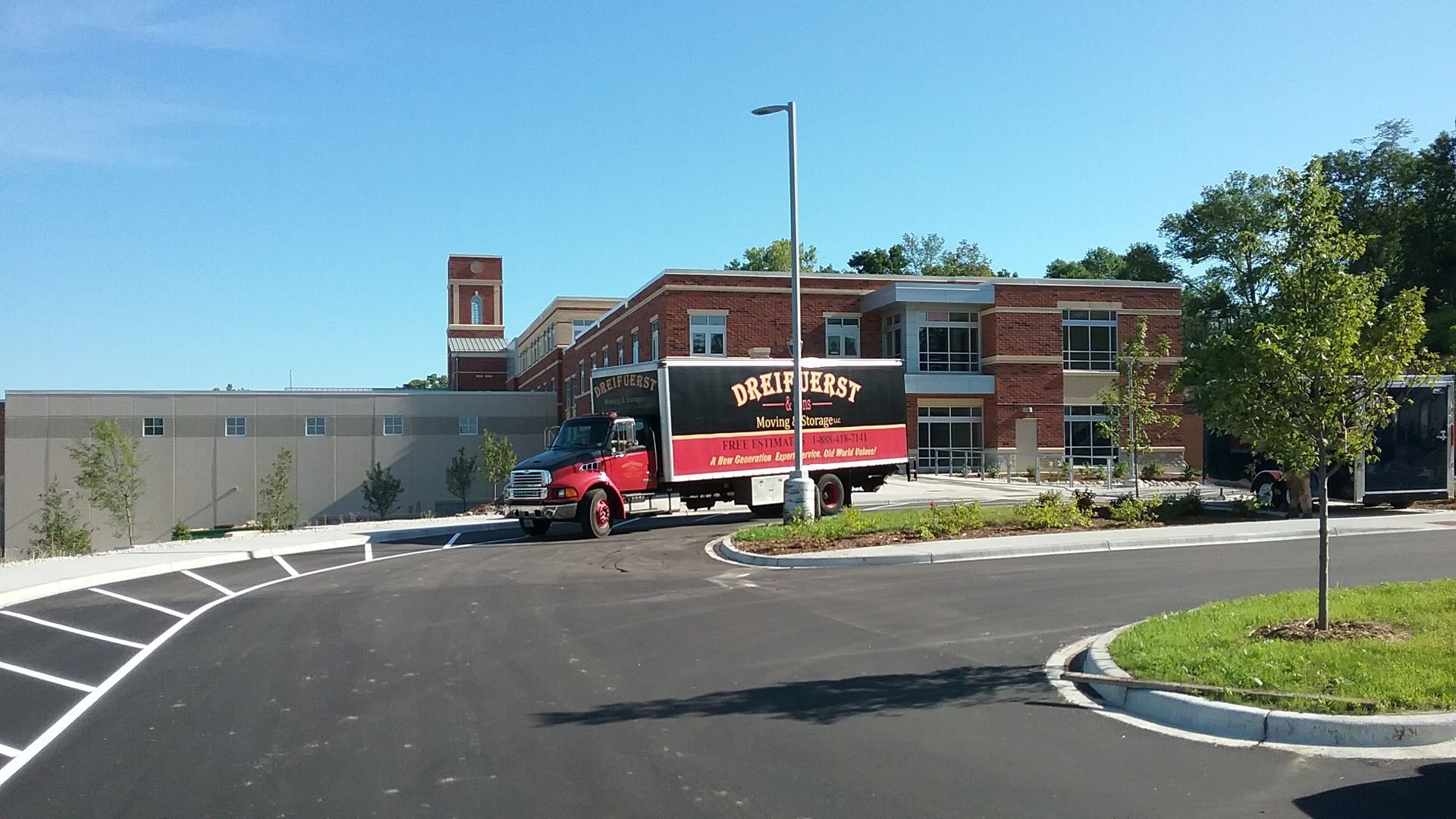 Red moving truck parked in front of a brick building on a sunny day.