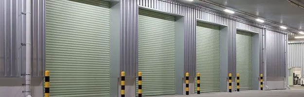 Row of closed roll-up doors, likely storage units. Metal construction, with floor-to-ceiling frames, neutral colors.