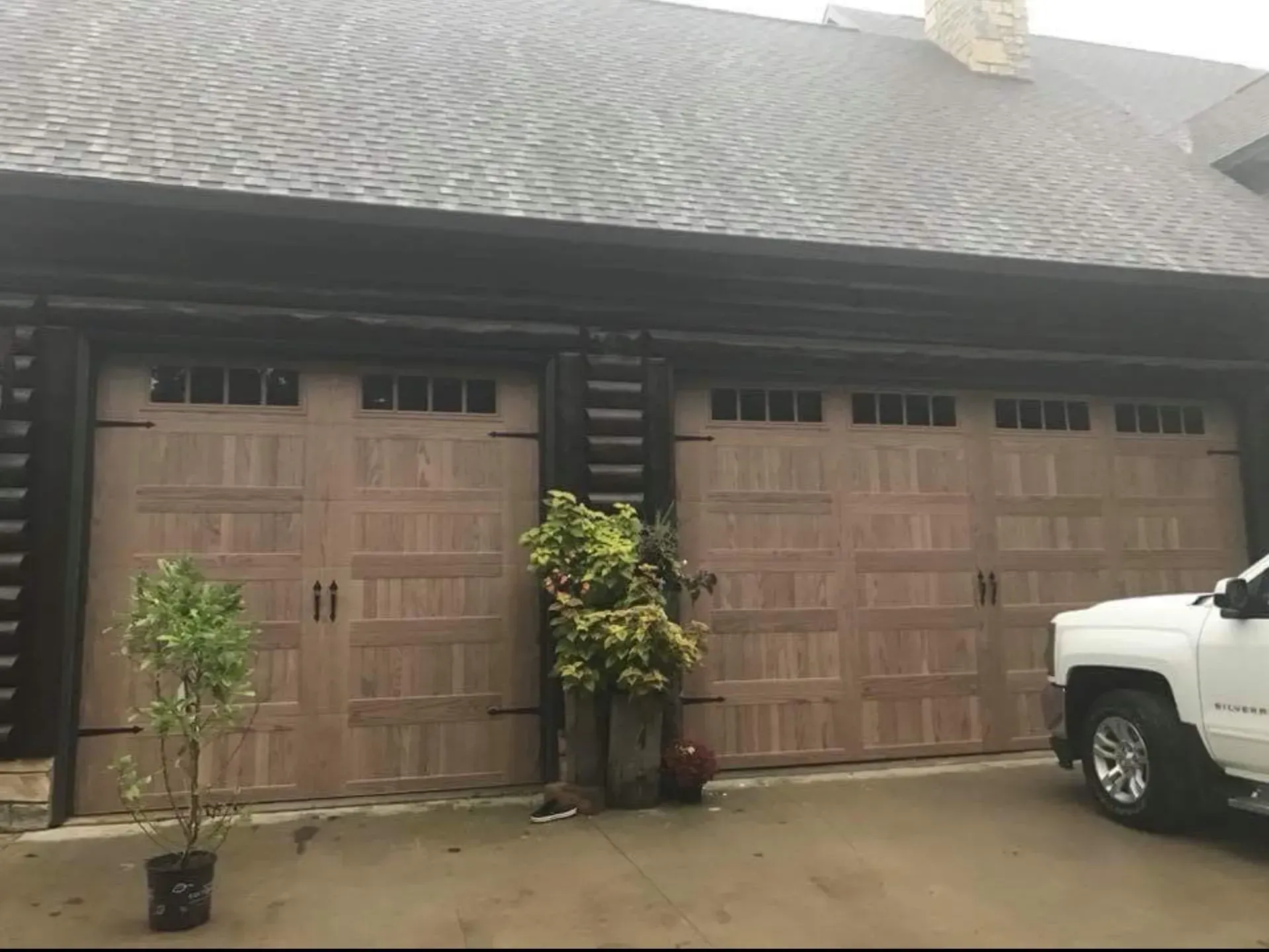 Two brown garage doors on a house with a dark roof; a white truck is partially visible.