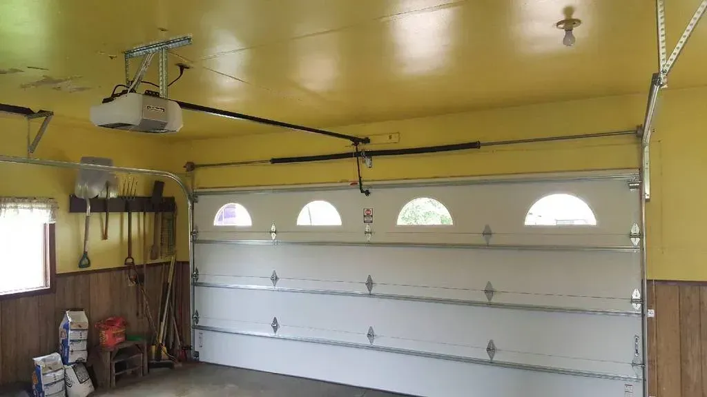 Garage interior with white garage door, yellow ceiling, and tools hanging on the wall.