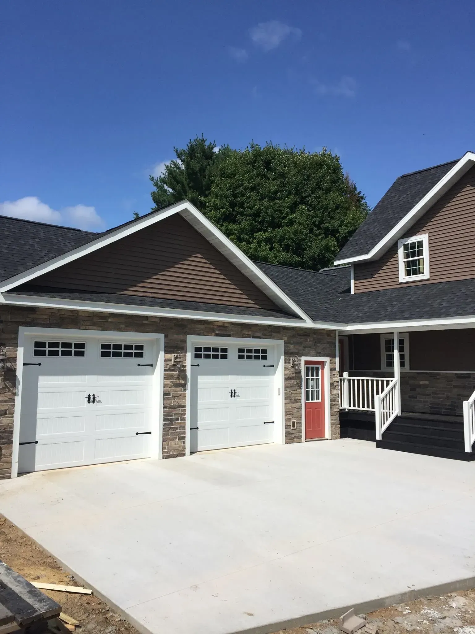 Two-car garage with brick veneer, white doors, and a red side door. Sunny day, blue sky.