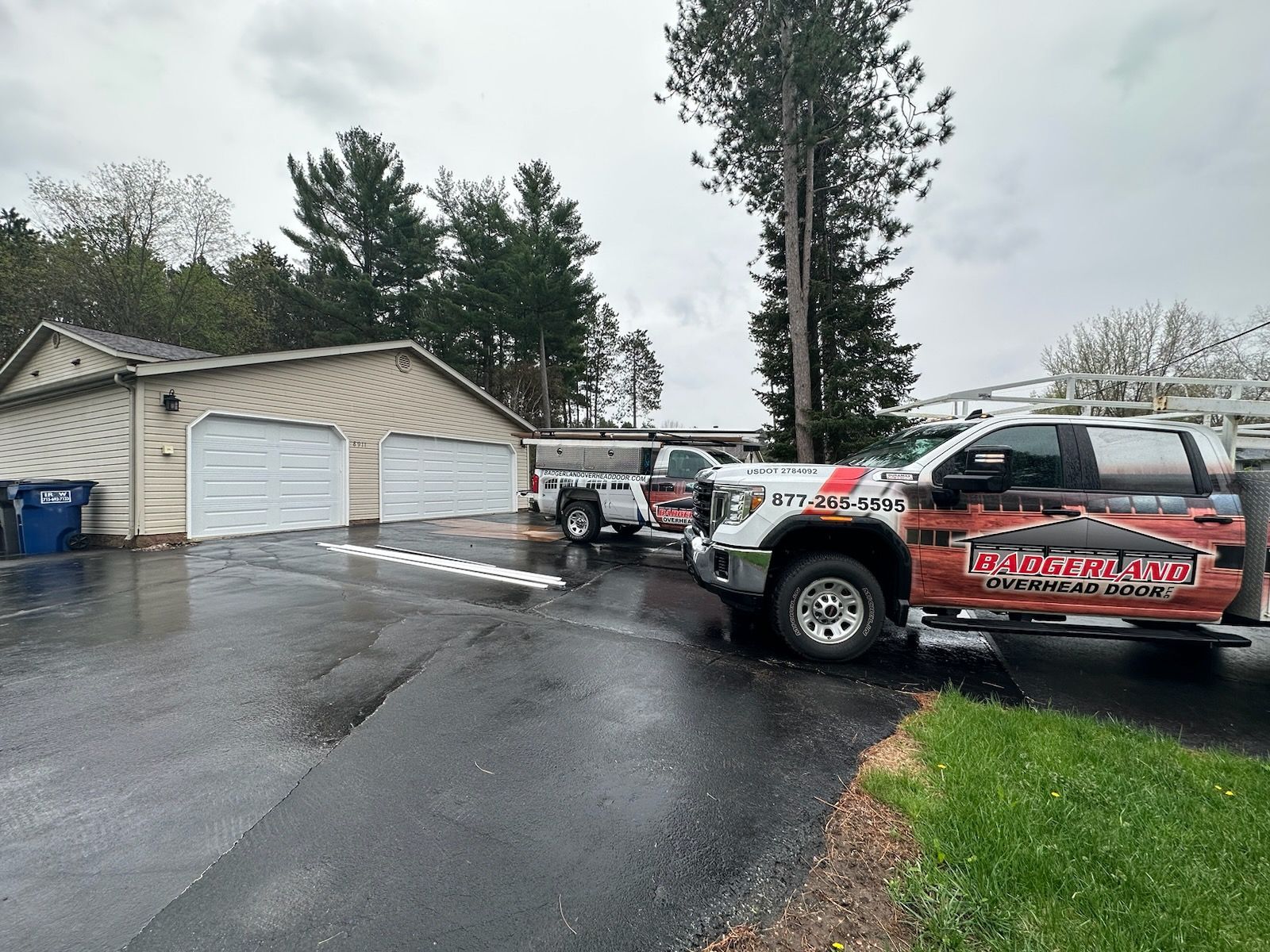 A driveway with commercial trucks parked in front of a garage on a cloudy day.