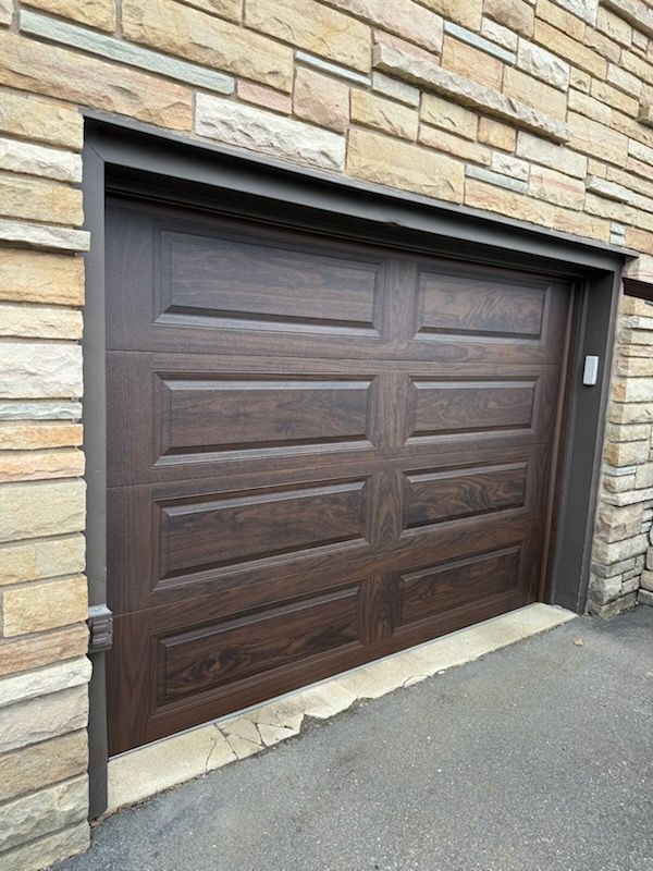 Brown garage door with dark trim, set in a stone wall.