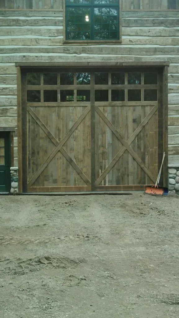 Wooden double garage doors with decorative X design, topped with small window panes, set in log cabin exterior.