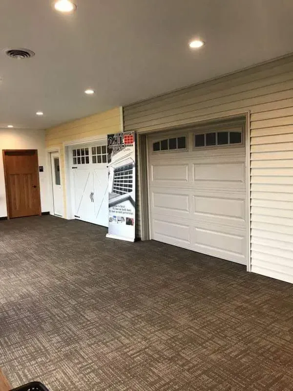 Room with carpet, displaying two white garage doors with different siding samples.