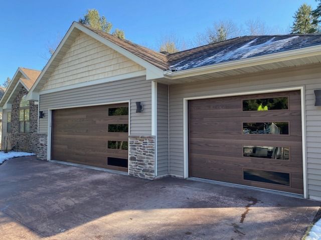 Two brown modern garage doors with rectangular windows, flanked by stone and tan siding.
