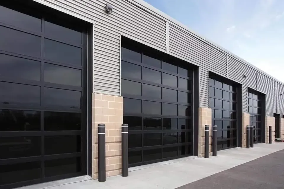 Black glass garage doors on a modern building with silver siding and brick accents.