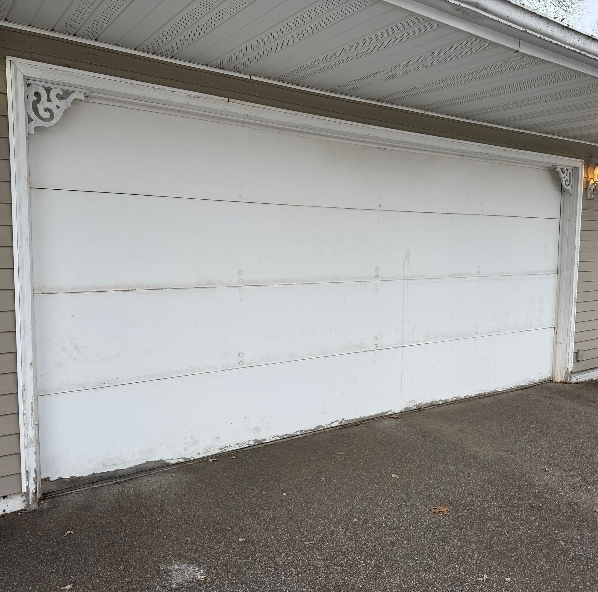 White garage door on a gray driveway, with decorative brackets at the top corners.