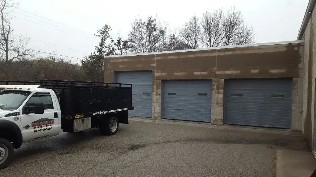 A work truck parked in front of a building with three gray garage doors.