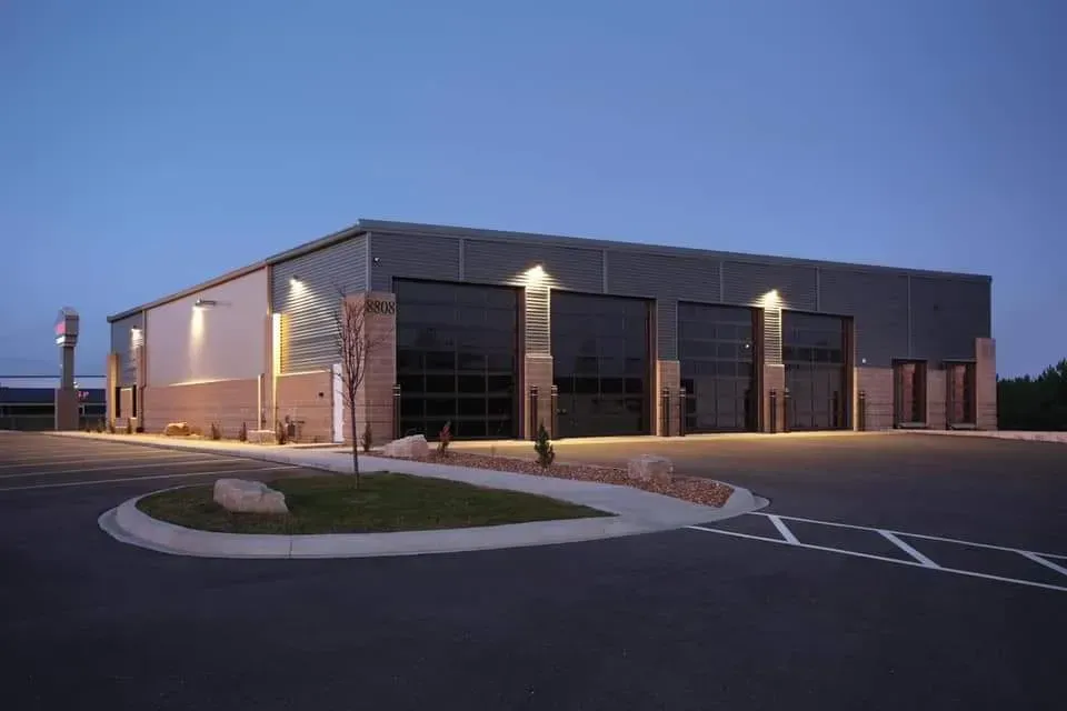 Modern commercial building with three large garage doors, paved lot, and dusk sky.