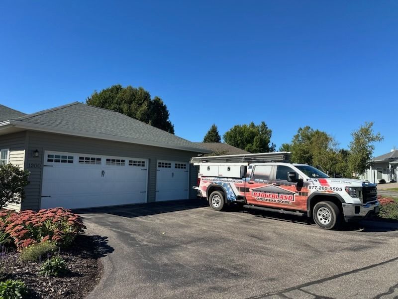 A white truck with company branding parked in front of a house with a two-car garage on a sunny day.