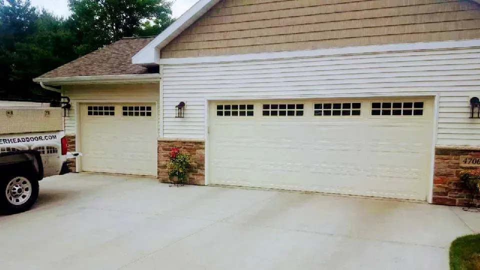 Two white garage doors with windows, tan siding, and stone accents.