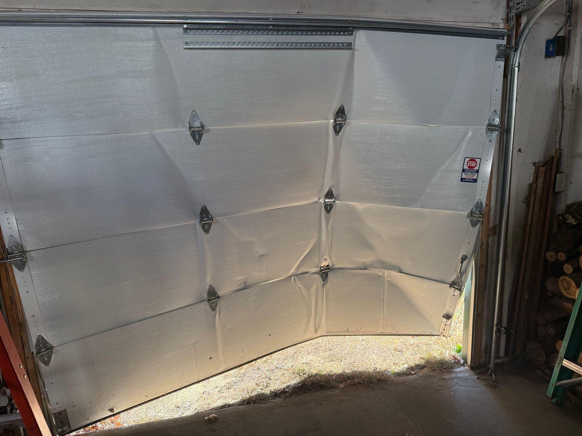 Damaged white garage door, partially open and dented, likely from impact.