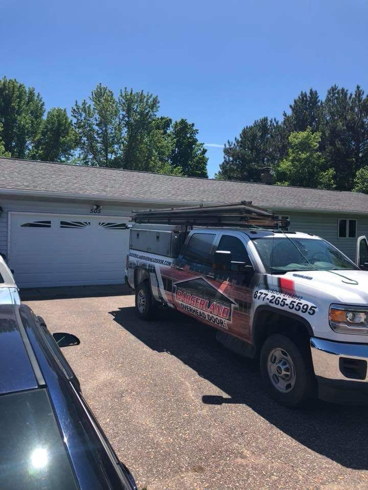 A white truck with business logos parked in a driveway in front of a gray garage on a sunny day.