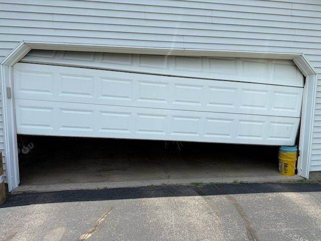 White garage door, one side collapsed, partially open. A yellow bucket supports the door.