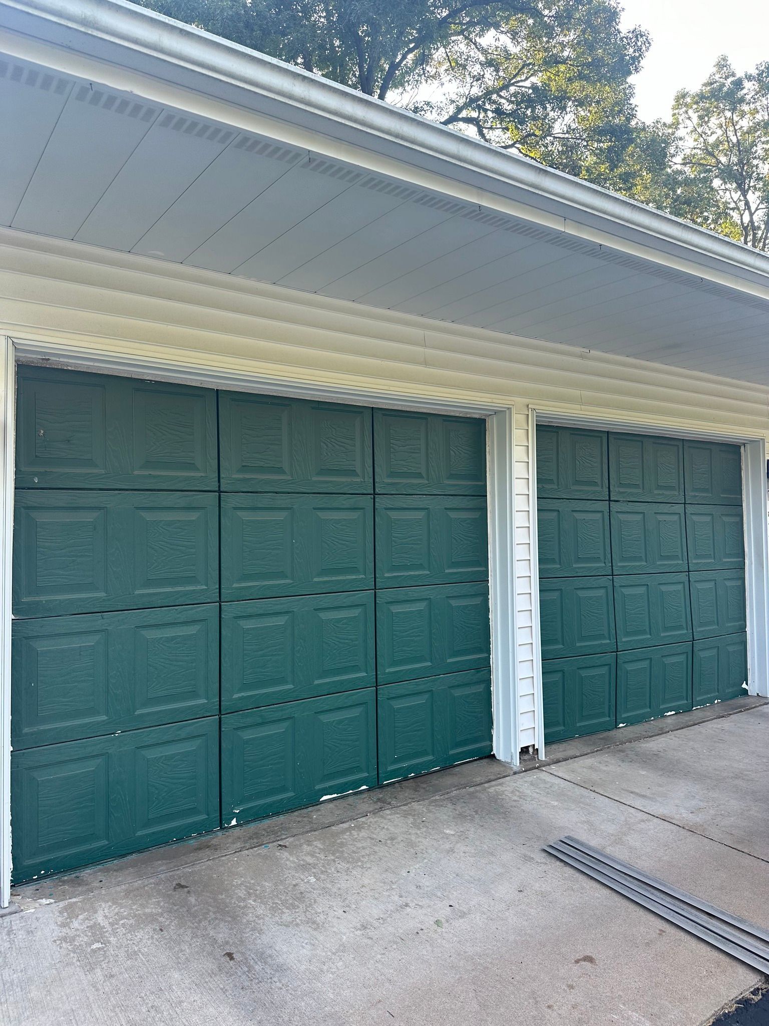 Green garage doors on a gray concrete driveway, under a white soffit.