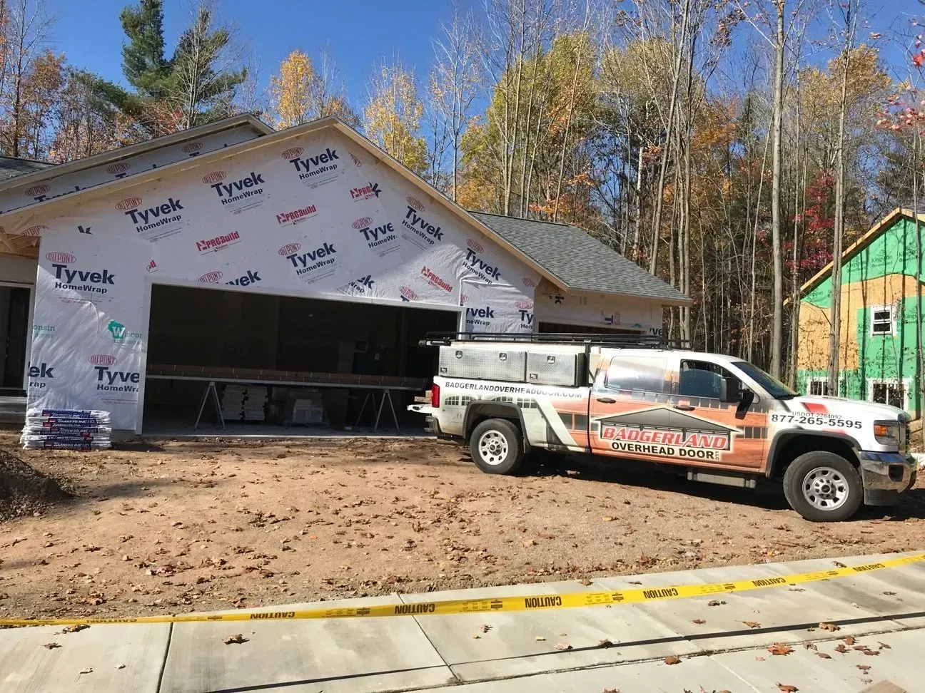 Construction site: partially built garage, white truck parked in front, Tyvek wrap visible.